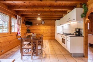 Un interior de madera con cocina, mesa de comedor, sillas y un reloj en la pared.