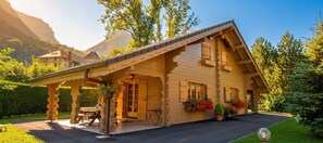A wooden chalet with a sloped roof, a covered patio with a table and chairs, and a garden with potted plants. - Chalet 'Mitoyen 4 Personnes' with Mountain View, Private Terrace and Wi-Fi (Alex)