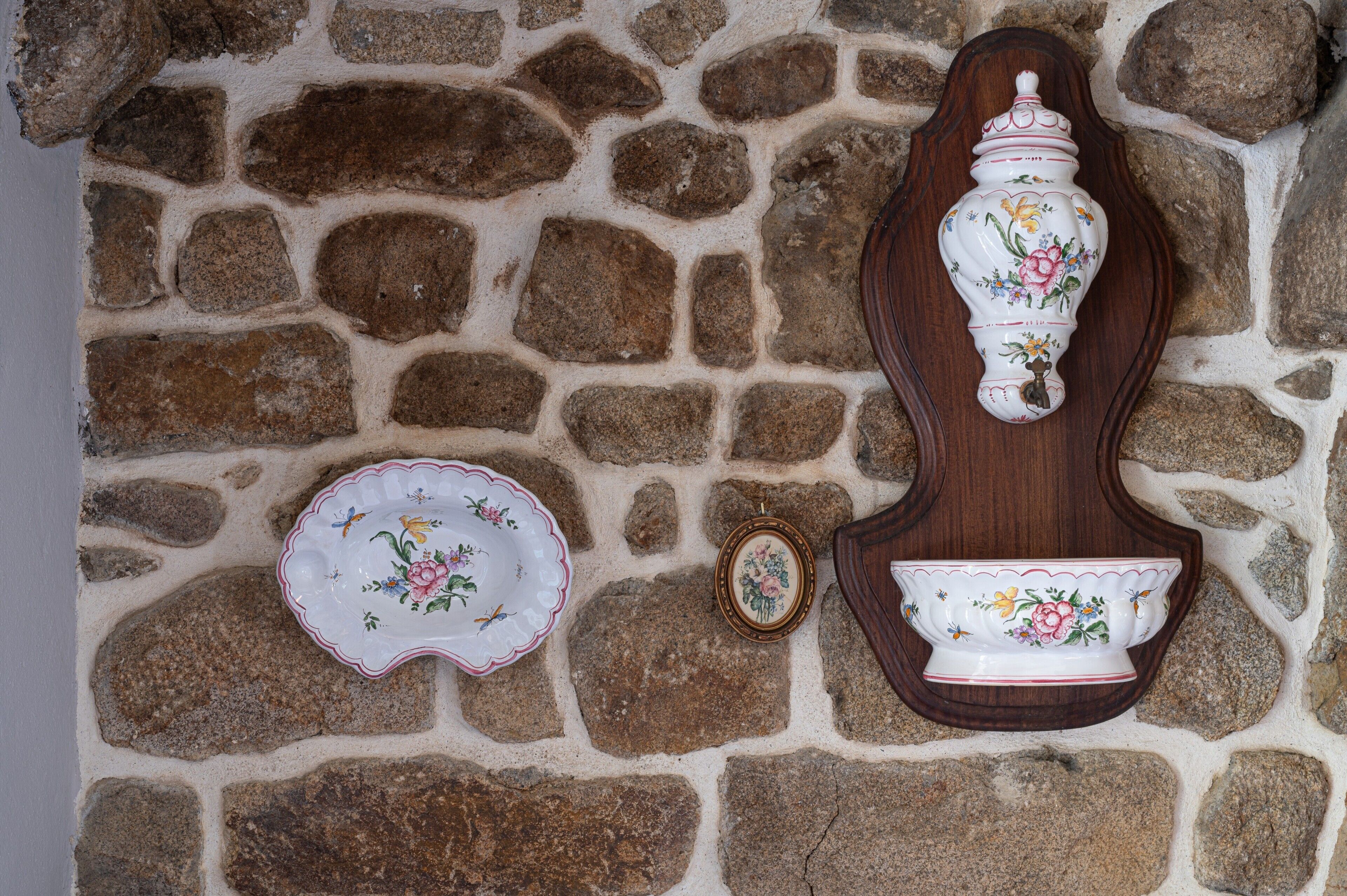 Mural de pedra com um vaso de cerâmica decorativo e uma pequena travessa fixadas nele.