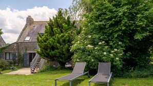 Un bâtiment en pierre avec un toit en pente, un escalier en bois et deux chaises longues en métal, le tout situé dans un espace verdoyant.