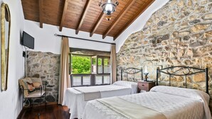 Un dormitorio con dos camas, paredes de piedra, vigas de madera, un televisor y una ventana con vistas.