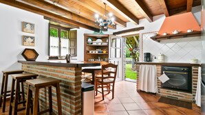 Una cocina con salpicadero de ladrillo, taburetes de madera, una isla central y una lámpara colgante.