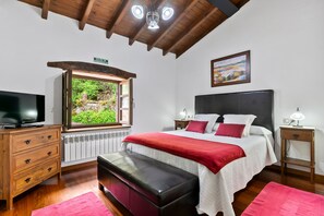 Ein Schlafzimmer mit einem großen Bett, einem Fernseher, einer Bank, einem Fenster mit Aussicht, einem Nachttisch und einem Bild an der Wand.