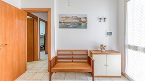 Ein Zimmer mit einer hölzernen Bank, einem kleinen Schrank, einem gerahmten Bild an der Wand und einer Tür zu einem weiteren Raum.
