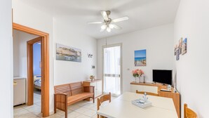 Ein Zimmer mit Esstisch, einer hölzernen Bank, Deckenventilator, Fernseher und Bildern an den Wänden.