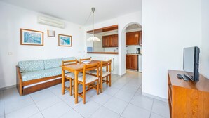 Ein Wohnzimmer mit einer Couch, einem Esstisch, Stühlen, einem Fernseher und einer Küche im Hintergrund.