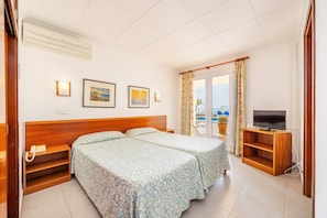 Habitación de hotel con dos camas, un mueble para televisión y vista al mar.