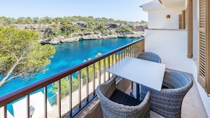 A balcony with wicker furniture, a white table, and a view of the sea and rocky landscape.