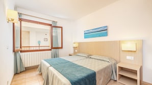 A bedroom with a bed, bedside tables, a mirror, a picture on the wall, and a window with curtains.