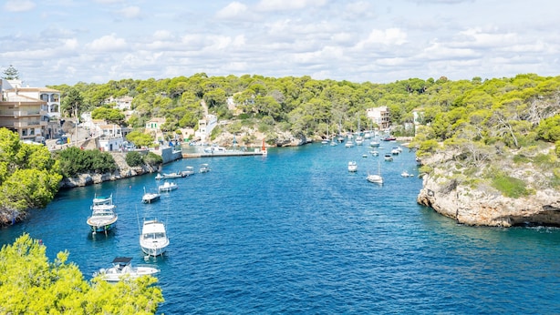 A coastal town with boats docked along a narrow waterway, surrounded by greenery and buildings.