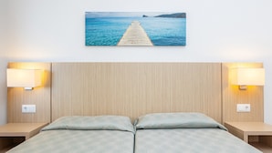 A double bed with a patterned bedspread, two bedside lamps, a wall-mounted power outlet, and a framed picture of a pier extending into a body of water. - Apartment 'Vista Al Mar Y Vista Puerto' with Sea View, Wi-Fi and Air Conditioning (Cala Figuera)