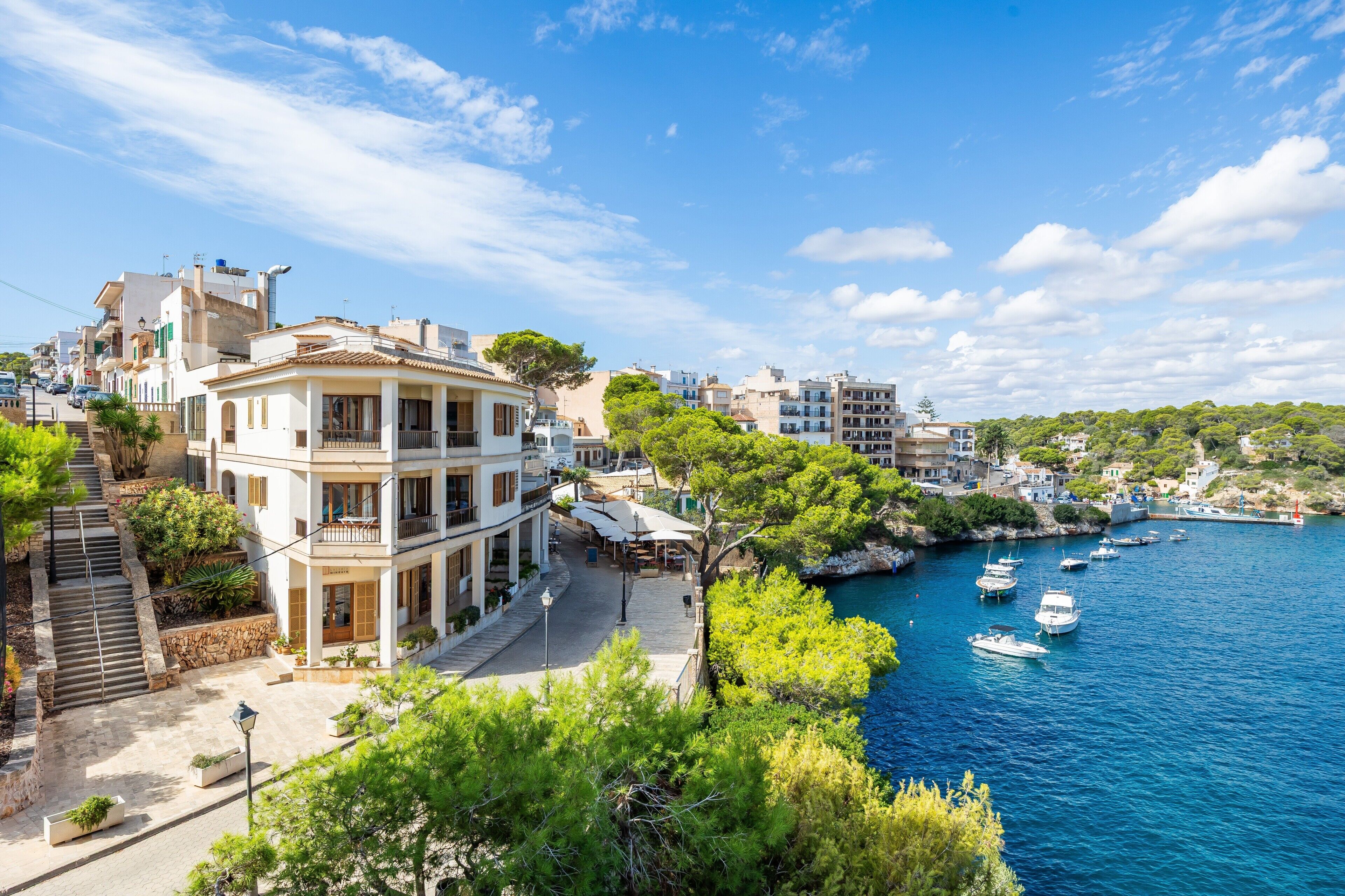 Une ville côtière qui se distingue par un imposant bâtiment blanc doté de balcons, un front de mer où sont amarrés des bateaux et une colline parsemée de bâtiments résidentiels.