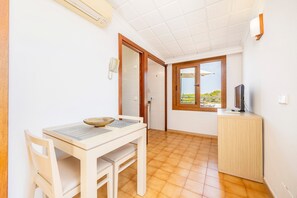 A compact room with a dining table, chairs, a small cabinet, a television, and a window with a view.