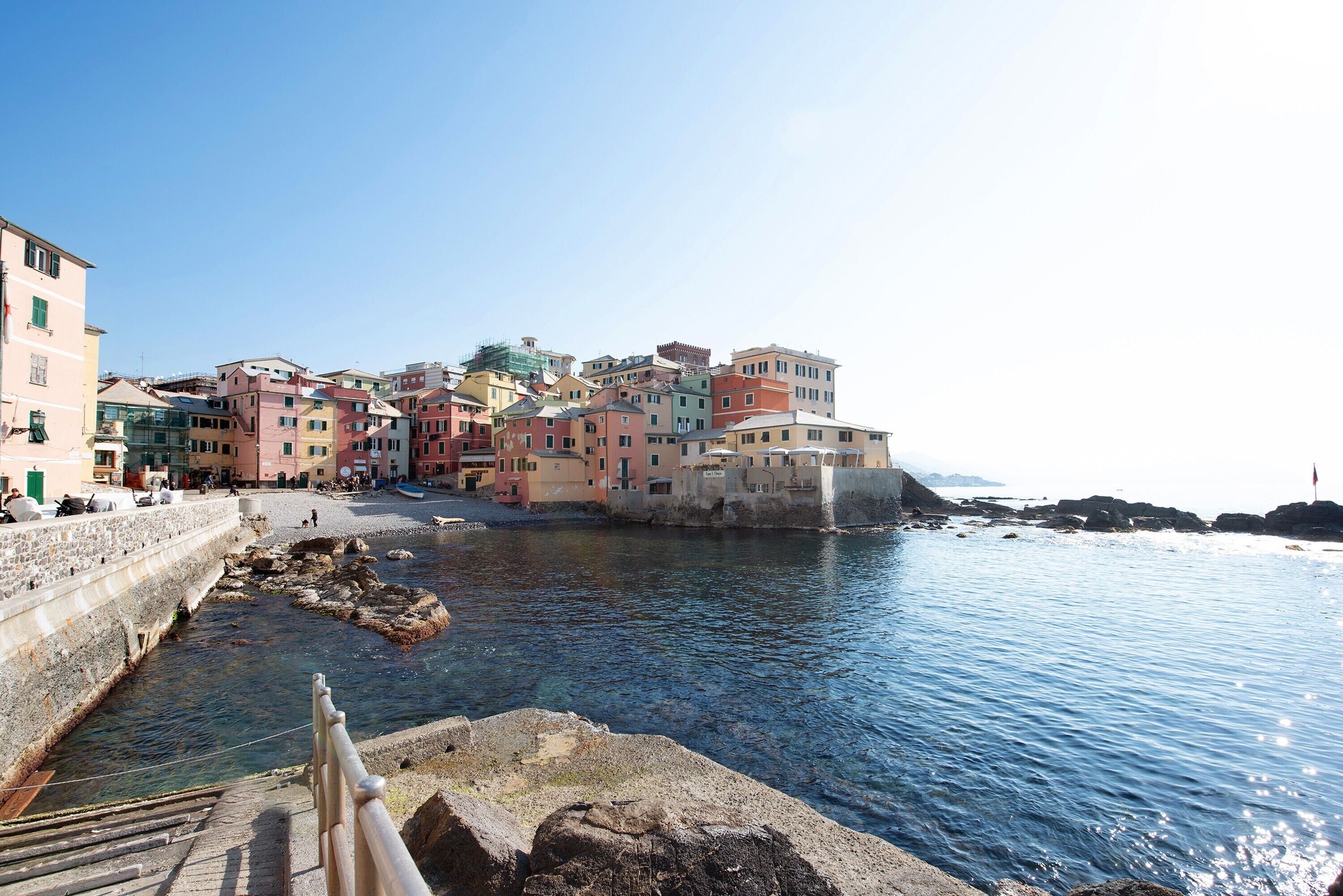 A coastal town with colorful buildings, a stone wall, and a calm sea.