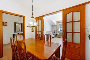 Ein Essbereich mit Holztisch und Stühlen, einer Pendelleuchte und Blick in ein Wohnzimmer mit Sofa und Fenster.
