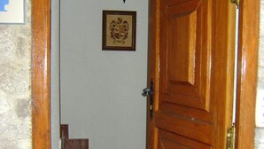 Una puerta de madera con un tirador de latón, un escudo heráldico enmarcado en la pared y un tramo de escaleras de madera que conducen a una habitación.