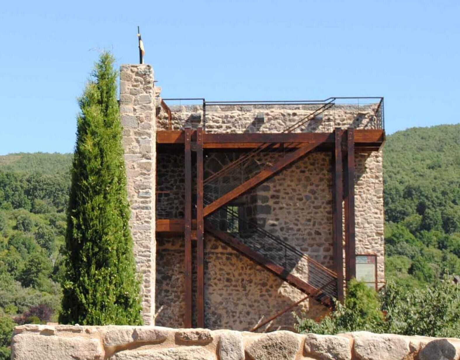 Un edificio de piedra con una escalera de metal y vistas a una ladera boscosa.