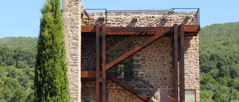 A stone building with a metal staircase and a view of a forested hillside.