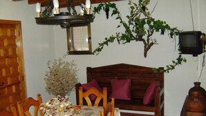 Comedor con una mesa lista para cuatro personas, un banco de madera, una araña, un televisor y una vid colgante.