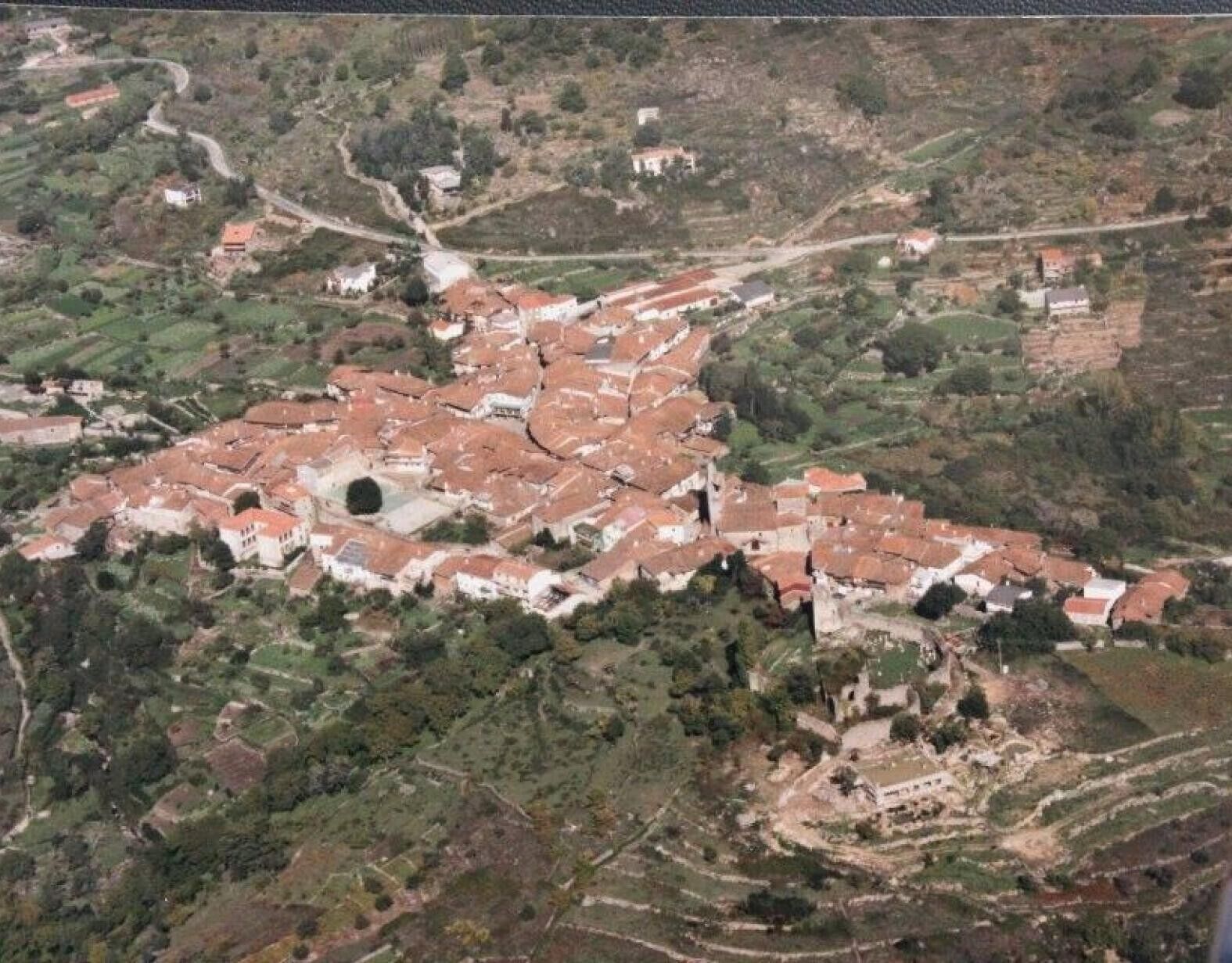 Une vue aérienne d’une ville dont le centre est constitué d’un ensemble de bâtiments, entouré de champs en terrasses et de maisons dispersées.