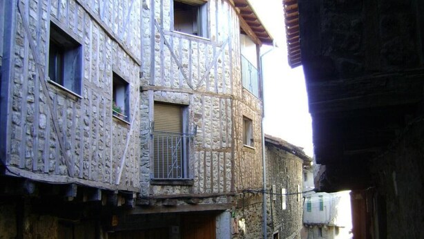 Un edificio de piedra con puerta de madera, un balconcito y una planta en maceta.