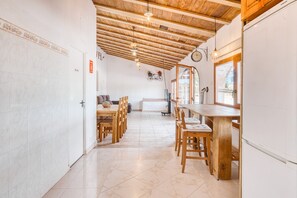 A kitchen with wooden cabinets, a refrigerator, and a dining area with chairs and a table. - Chalet 'Casa Stone' with Mountain Views, Private Pool and Wi-Fi (Alicante)