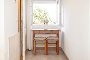 A wooden desk with two chairs, a window with a view of greenery, and a white wall. - Vacation Home 'Kassiopea' with Private Pool, Private Terrace and Wi-Fi (Ciutadella de Menorca)