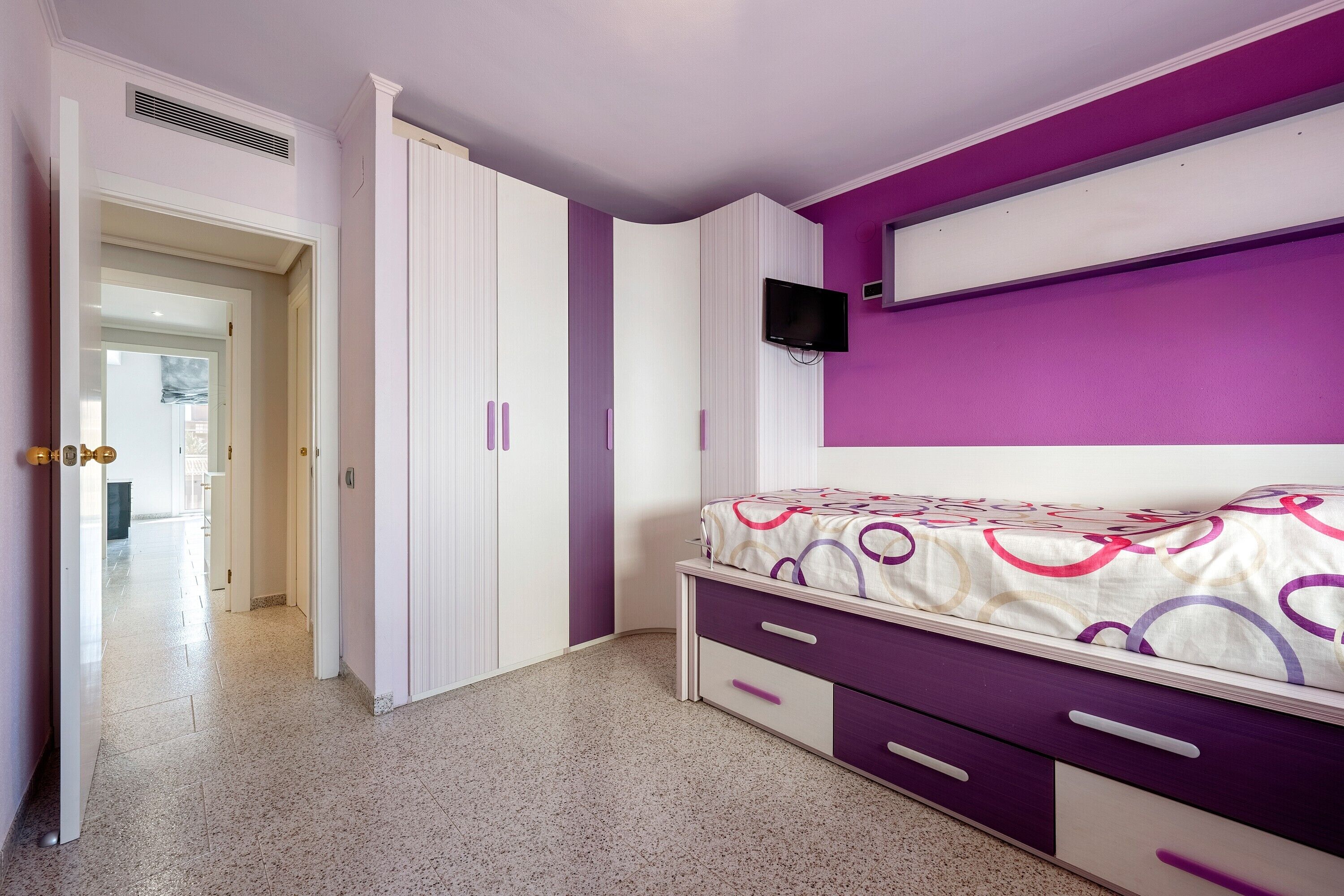 Un dormitorio con cama, armario, televisor y un pasillo que conduce a otra habitación.