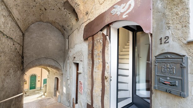 Un estrecho callejón con una puerta verde, un buzón y una escalera que lleva a un nivel superior.