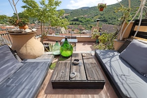 Une terrasse sur le toit, avec une table en bois, deux canapés et un grand bac à plantes contenant des rochers et une plante en pot.