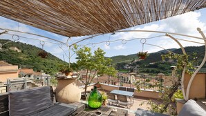 Una terraza con mesa de madera, sofá y macetas colgantes.