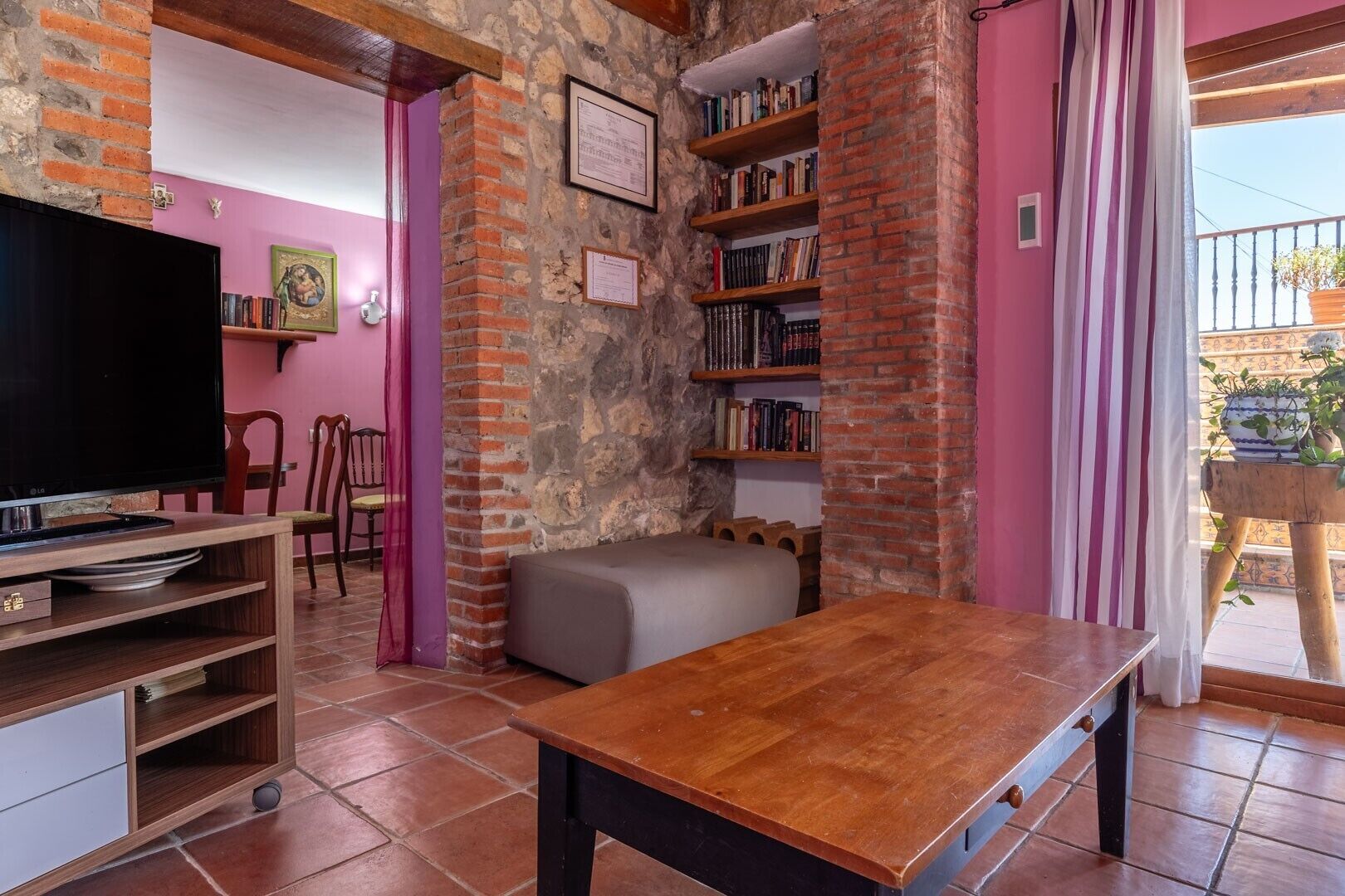 A room with a TV, wooden furniture, a bookshelf, and a stone wall.