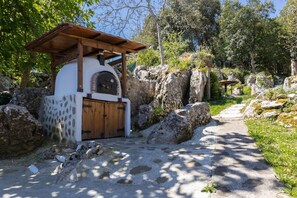 A rustic stone building with a wooden door and a covered entrance, surrounded by large rocks and greenery. - Holiday Home 'Posada Paraso Iris' with Mountain View, Private Garden and Wi-Fi (Isla)
