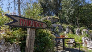 A wooden signpost with the word 'MIRADOR' in red, a rustic table with a bowl, and a rocky landscape with greenery.
