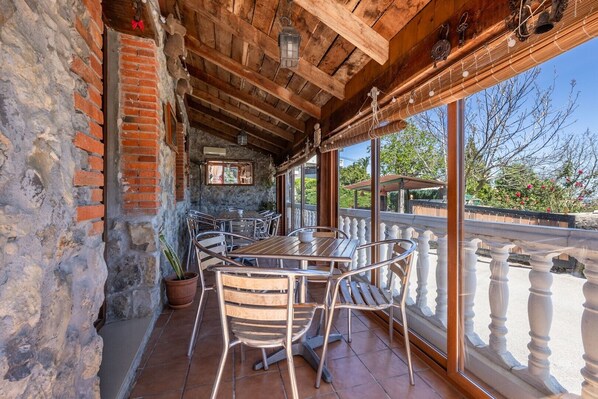 A covered outdoor seating area with a brick wall, metal chairs, a wooden table, and a view of the outdoors. - Holiday Home 'Posada Paraso Iris' with Mountain View, Private Garden and Wi-Fi (Isla)