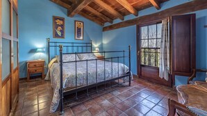 A bedroom with a wooden ceiling, a bed with a metal frame, a nightstand, a chair, and a window with curtains.