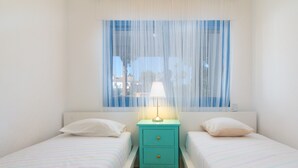 A room with two beds, a nightstand with a lamp, and a window with sheer curtains. - Apartment 'Duquesa Suites Golf and Gardens' with Shared Pool, Wi-Fi and Air Conditioning (Manilva)