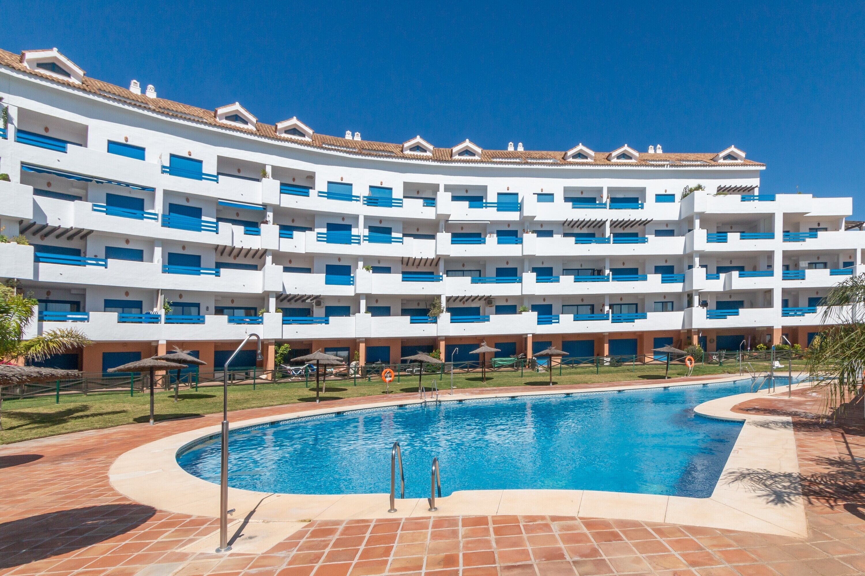Un hôtel à plusieurs étages doté d’une piscine, de parasols et offrant une vue sur un ciel bleu dégagé.