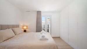 A modern hotel room with a large bed, a bedside table with a lamp, and a view of the outside through a window. - Holiday Home 'Townhouse El Naranjal' with Sea View, Wi-Fi and Air Conditioning (Marbella)