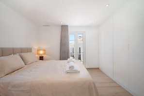 Camera d'hotel moderna con un letto grande, un comodino con una lampada e vista all'esterno da una finestra.