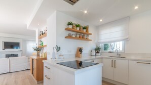 A modern kitchen with white cabinetry, wooden shelves, and a central island. - Holiday Home 'Townhouse El Naranjal' with Sea View, Wi-Fi and Air Conditioning (Marbella)