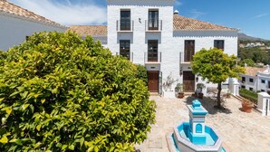 A white building with a tiled roof, a courtyard with a fountain, and surrounding greenery. - Holiday Home 'Townhouse El Naranjal' with Sea View, Wi-Fi and Air Conditioning (Marbella)