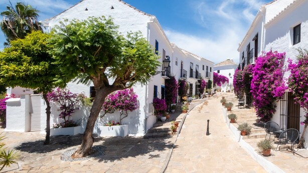 A narrow street lined with white buildings, potted plants, and outdoor seating. - Holiday Home 'Townhouse El Naranjal' with Sea View, Wi-Fi and Air Conditioning (Marbella)