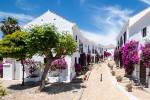 A narrow street lined with white buildings, potted plants, and outdoor seating.