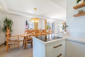 Eine moderne Küche mit einer zentralen Kochinsel, Holzkstühlen, einem Esstisch und einer Pendelleuchte.