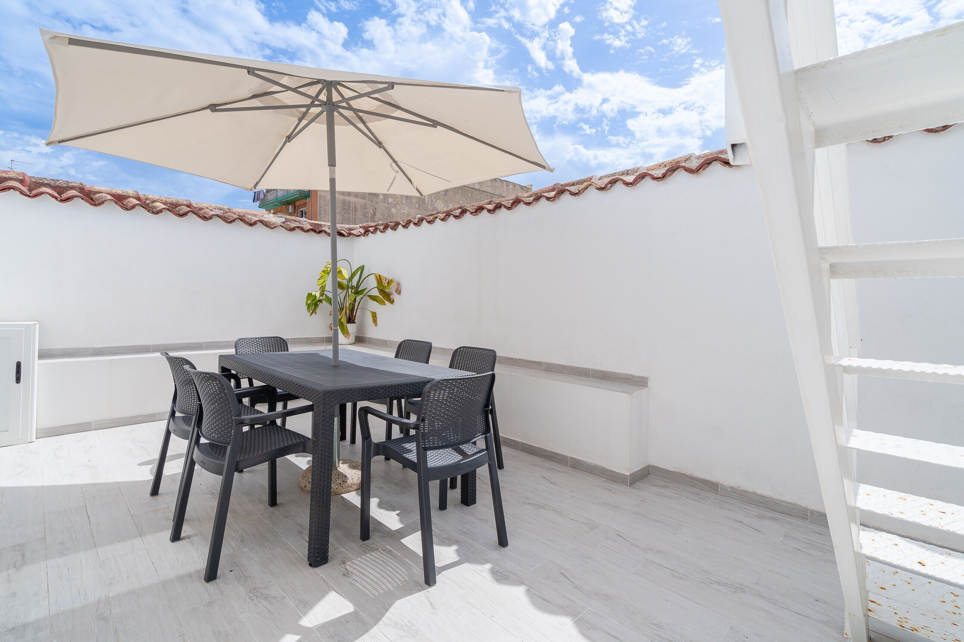 Une terrasse extérieure avec une table et des chaises, un grand parasol et une plante en pot.