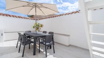 Une terrasse extérieure avec une table et des chaises, un grand parasol et une plante en pot.