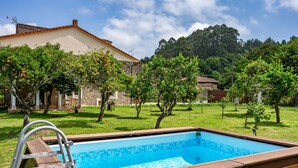 Une piscine dotée d’une terrasse en bois et d’un escalier en métal, entourée d’une pelouse et de quelques arbres fruitiers.
