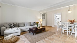 Un salon comprenant un canapé, une table basse, une table à manger et des chaises. On y trouve également un meuble et une lampe.