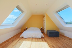 A bedroom with a sloped ceiling, skylights, a bed, bedside tables, and a bench.